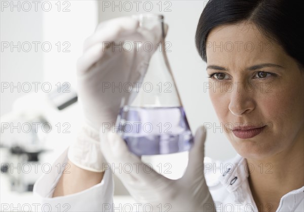 Female scientist looking at liquid in beaker.