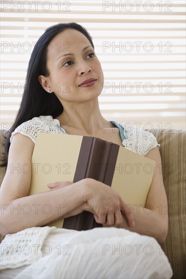 Asian woman holding book on sofa.