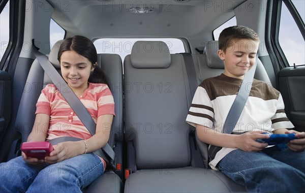 Brother and sister playing video games in car.