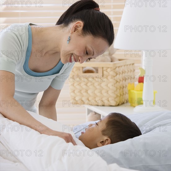 Asian mother tucking son into bed.