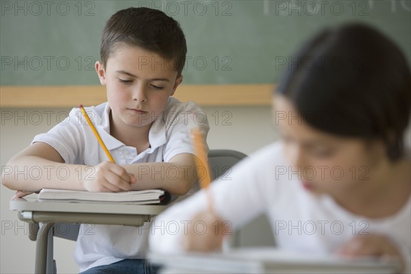 Boy writing at desk in classroom.