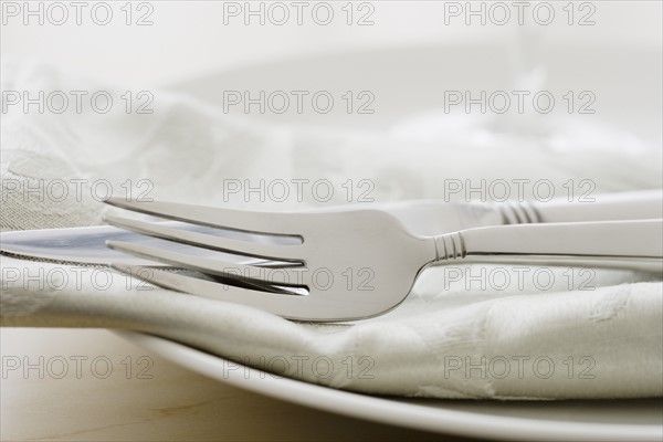 Close up of silverware and napkin on plate.