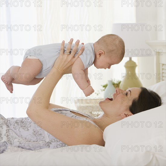 Mother playing with baby on bed.