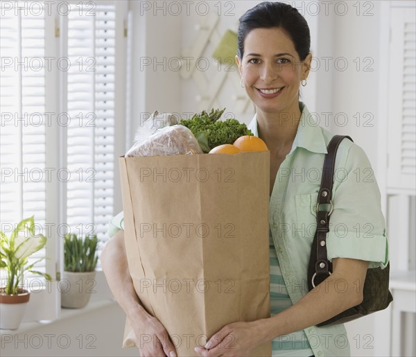 Woman holding bag of groceries in kitchen.