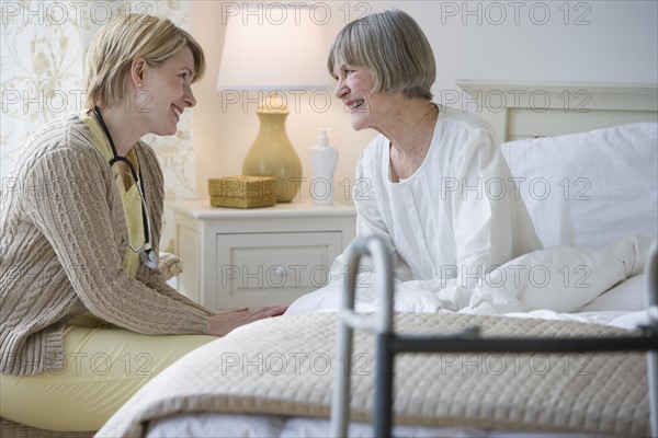 Nurse talking to senior woman in bed.