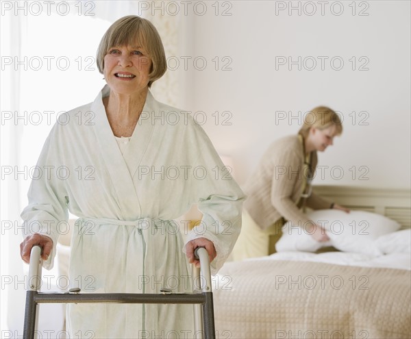 Senior woman using walker in bedroom.