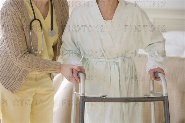 Nurse helping senior woman use walker.