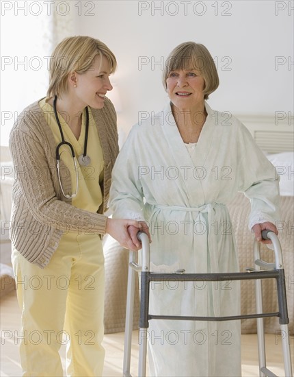 Nurse helping senior woman use walker.