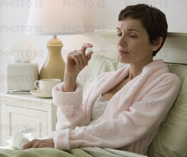 Woman taking own temperature in bed.