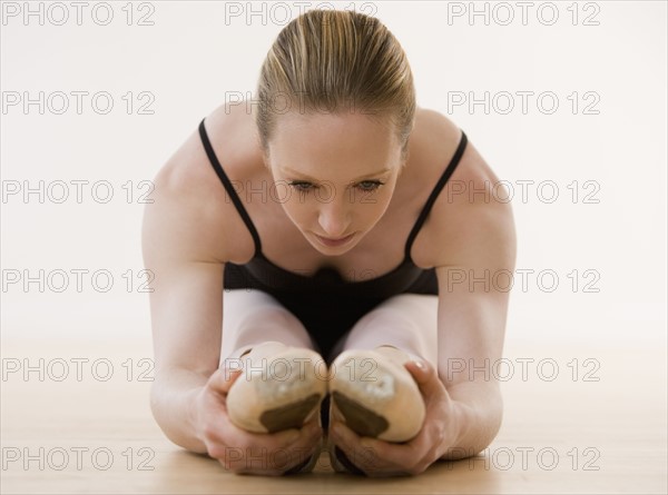 Female ballet dancer stretching on floor.