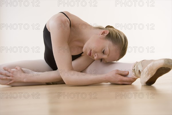 Female ballet dancer stretching on floor.