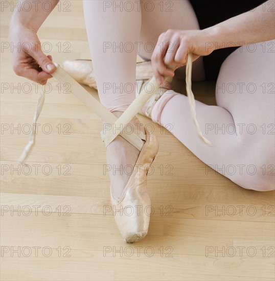 Female ballet dancer tying pointe shoes.