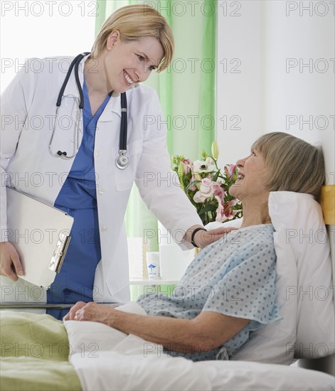 Female doctor talking to senior woman in hospital bed.