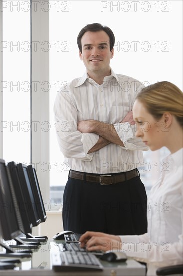 Businessman with arms crossed behind businesswoman.