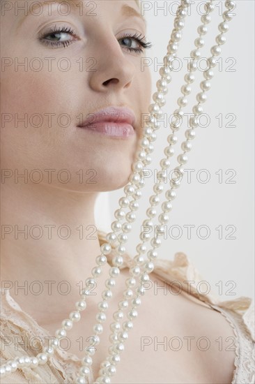 Woman with pearl necklace against face.
