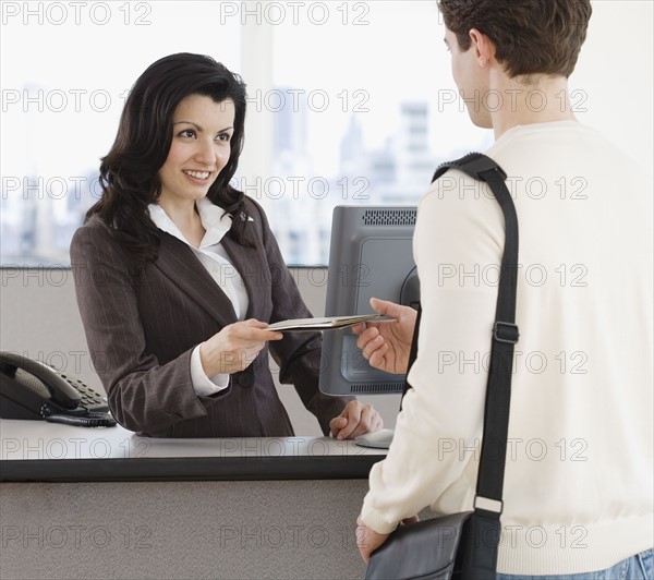 Woman handing paperwork over counter to man.