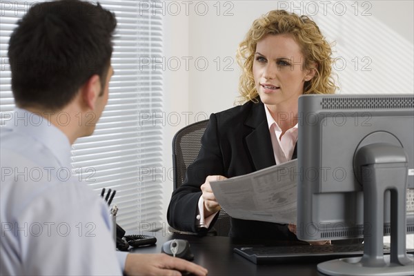 Businesswoman consulting with businessman at desk.