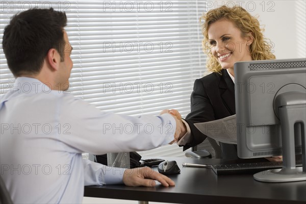 Businesswoman consulting with businessman at desk.