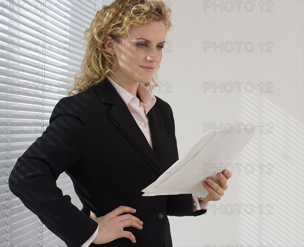 Businesswoman reading paperwork next to window.