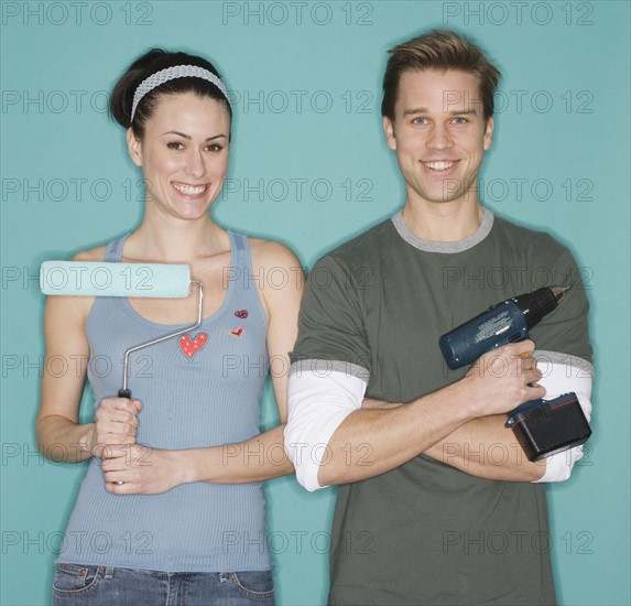 Portrait of couple holding paint roller and cordless drill.