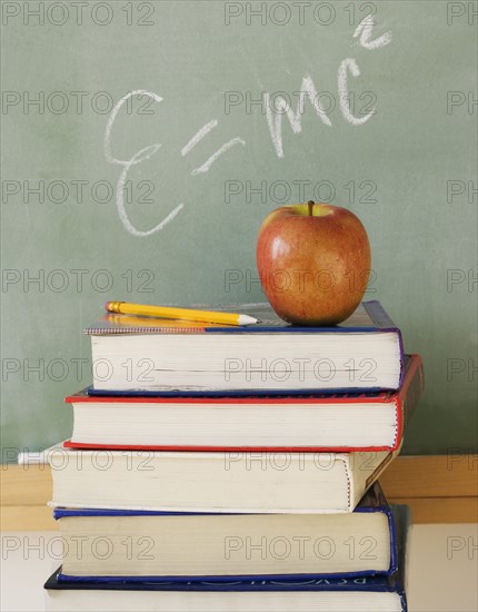 Stack of books and apple in classroom.