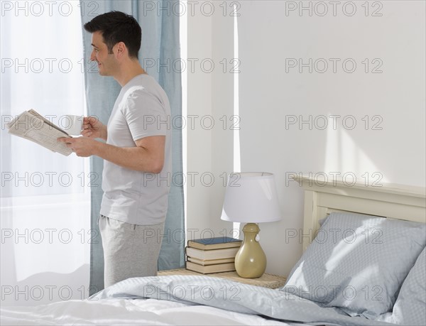 Man holding newspaper and coffee next to window.