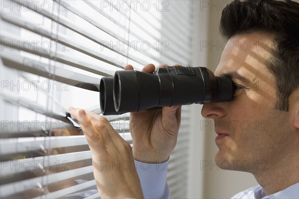 Businessman looking out window through binoculars.