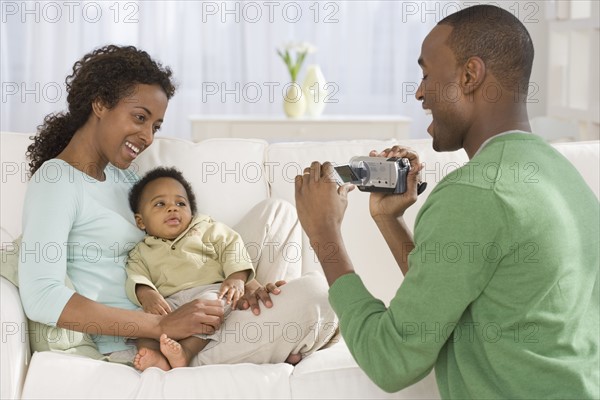 Father video recording mother and baby on sofa.