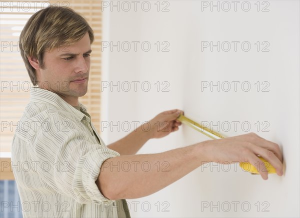 Man measuring wall with tape measure.