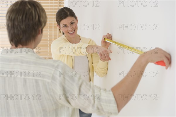 Couple measuring wall with tape measure.