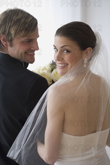 Portrait of bride and groom looking over shoulders.