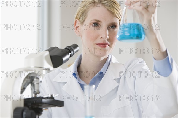 Female scientist looking at liquid in beaker.