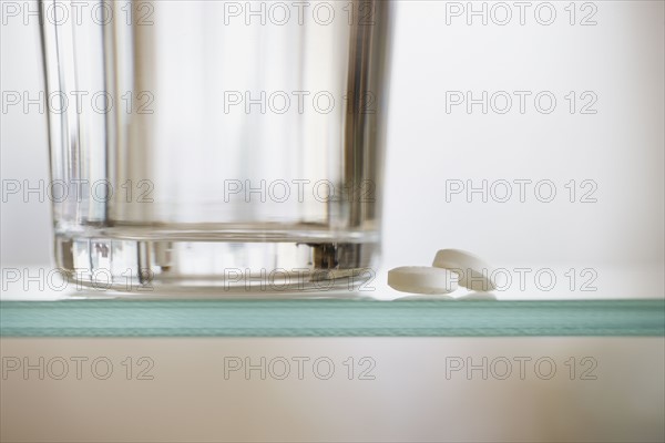 Medication and water glass on shelf.