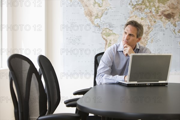 Businessman thinking next to laptop.