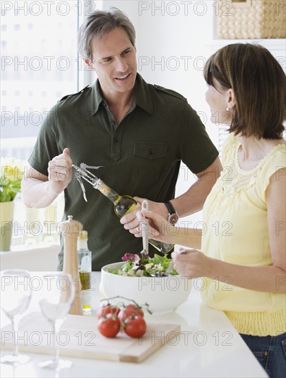 Couple tossing salad and opening wine.