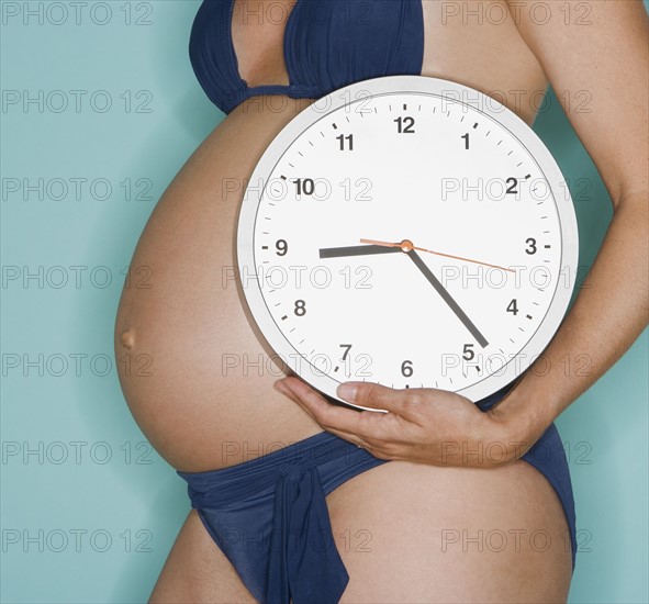 Pregnant woman holding wall clock.
