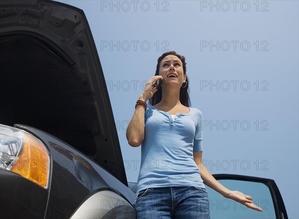 Woman talking on cell phone next to broken down car.