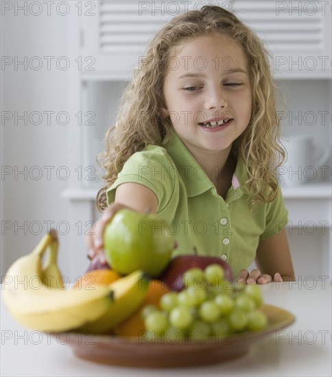 Girl reaching for fruit in bowl.