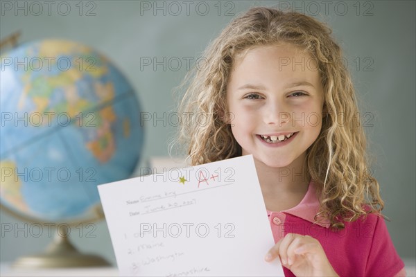 Girl holding up A plus paper in classroom.