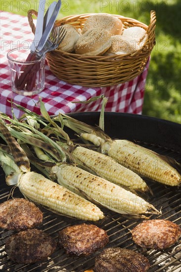 Corn and hamburgers cooking on grill.