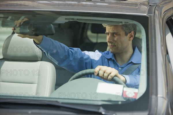 Man adjusting rear view mirror in car.