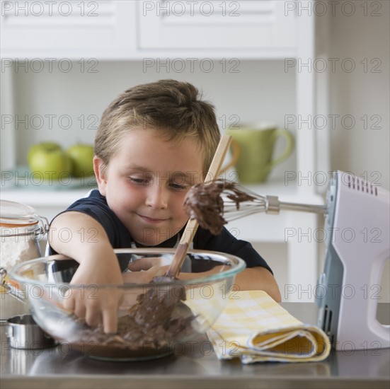 Boy sticking finger into bowl of batter.