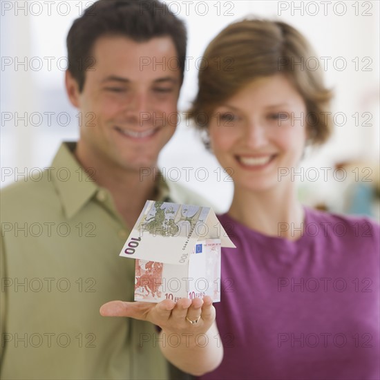 Couple holding model house made of Euro banknotes.