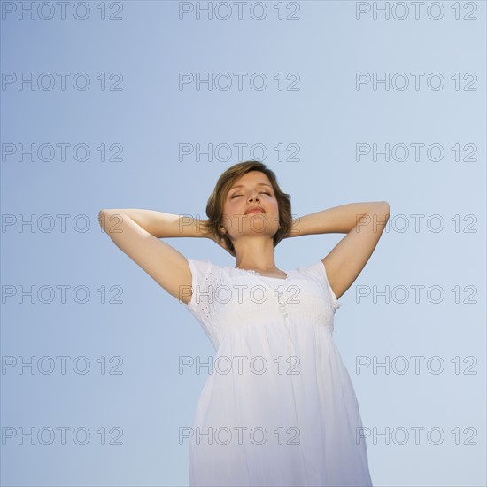 Low angle view of woman with arms behind head.