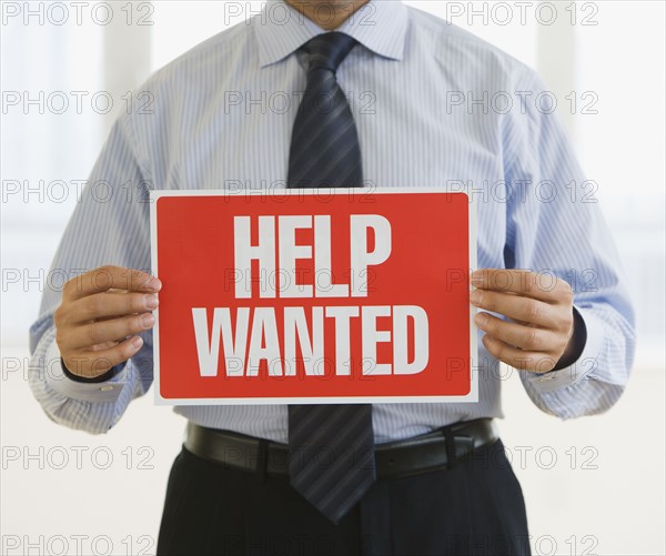 Businessman holding Help Wanted sign.