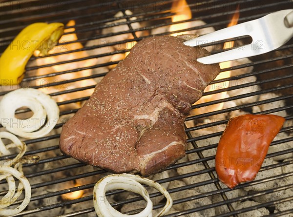 Steak and vegetables cooking on grill.