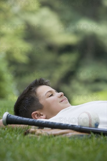 Boy laying in grass with baseball bat.