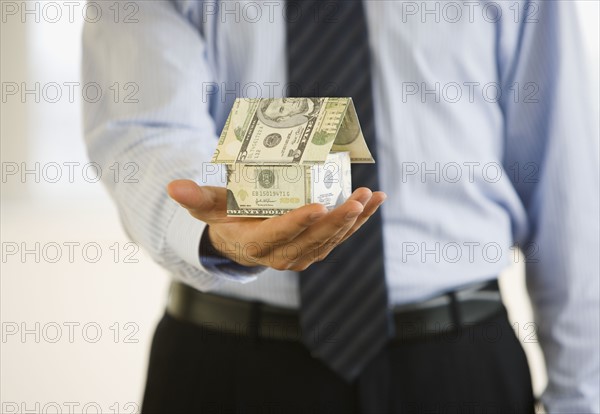 Businessman holding house made money.