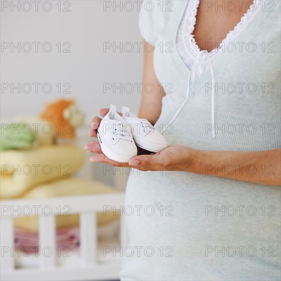 Pregnant woman holding baby shoes.