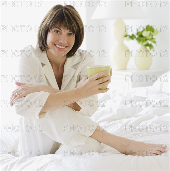 Woman sitting on bed holding coffee.